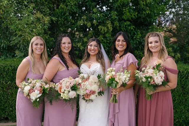 Bride in a white gown standing outdoors with four bridesmaids